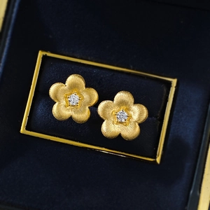 Macro detail of gold flower stud earrings with brushed texture and sparkling center stone