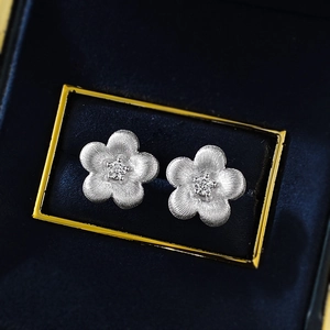 Macro shot of silver floral stud earrings with brushed texture and center cubic zirconia