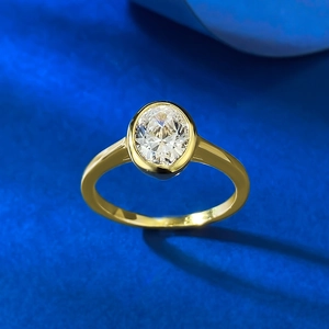 Close-up of a gold oval cut diamond ring featuring a bezel setting on a blue background
