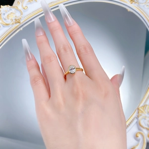 Macro shot of oval-cut diamond solitaire ring in a gold bezel setting worn on finger