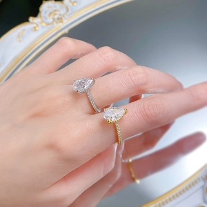 Macro detail of pear-shaped drop rings in silver and gold with pavé-set accents on hand