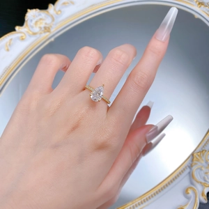 Detailed view of a pear-cut white stone ring with gold pavé band on a model hand