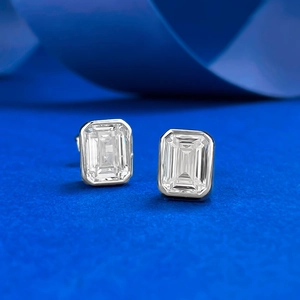 Macro view of emerald-cut white gemstone earrings in a classic silver bezel setting