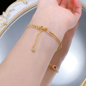 Détail d'un bracelet à perles plaqué or avec un charm en zircone sur un poignet féminin