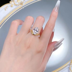 On-hand view of a gold V-shaped ring with a large oval-cut gemstone over a vintage mirror