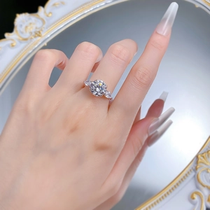 Détail de la bague en diamant rond avec pierres latérales poire au doigt devant miroir
