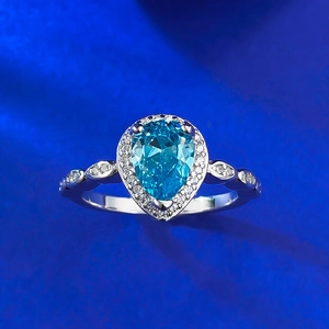 Close-up of pear-cut blue gemstone ring with halo diamonds on a dark velvet background