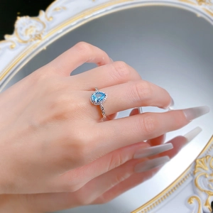 Close-up of elegant pear-shaped blue gemstone ring with halo diamonds on a woman's finger