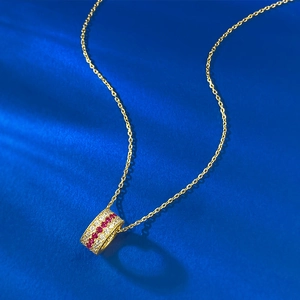 Close-up of golden cylinder pendant with red gemstones and white diamonds on blue silk