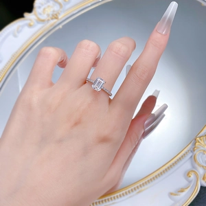 Detail of emerald cut gemstone ring with micro-pave band worn on female finger