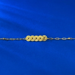 Detailed view of the gold coin bracelet on a deep blue silk texture background