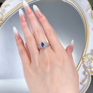 Close-up of a marquise-cut blue gemstone ring with micro-pave diamonds on a hand