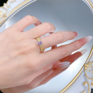 Vue macro de la bague nœud dorée avec pierre violette sur la main et reflet de miroir