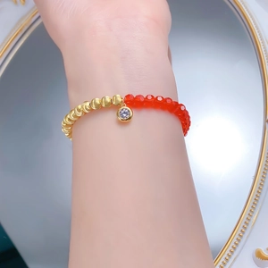 Détail du bracelet S925 doré avec perles rouges et pendentif en cristal sur le poignet