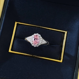 Sparkling oval pink gemstone ring with halo diamonds on a dark blue velvet box