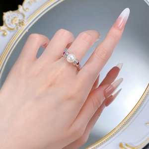 Macro detail of a vintage S925 silver pearl ring with red gems on a reflective mirror