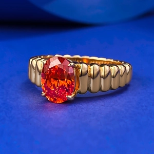 Dettaglio macro di anello con gemma arancione ovale e fascia dorata a coste su blu