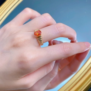 Dettaglio dell'anello con gemma arancione ovale e fascia dorata intrecciata sulla mano