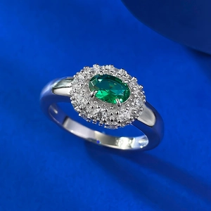 Macro shot of an oval emerald ring with double halo diamonds on a blue background