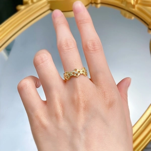 Close-up of gold hollow floral ring with zircons on finger next to a round mirror