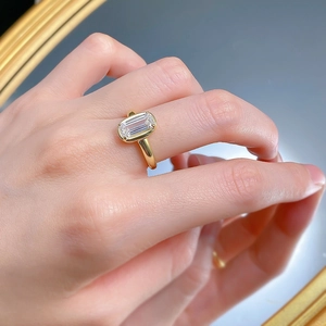 Detail of a gold rectangular step-cut cubic zirconia ring worn on a finger