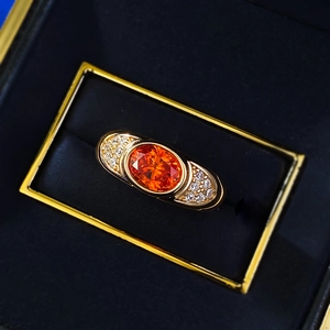 Macro detail of oval orange gemstone ring with diamond side stones in a black velvet box