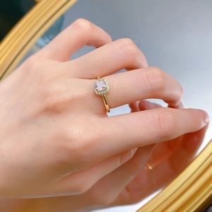 Gros plan d'une bague avec diamant rose de taille carrée et serti halo sur doigt doré