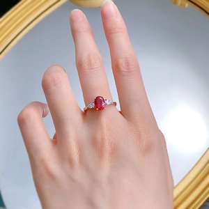 Detailed top view of an oval red corundum ring with pear-shaped side stones on a finger
