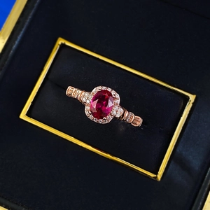 Macro shot of oval red gemstone ring with halo diamond setting on rose gold band