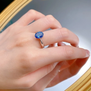 Detailed view of an oval blue sapphire ring on a hand featuring an elegant silver band