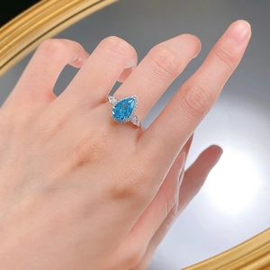 Side view of pear-shaped light blue gemstone ring with halo diamond setting on finger