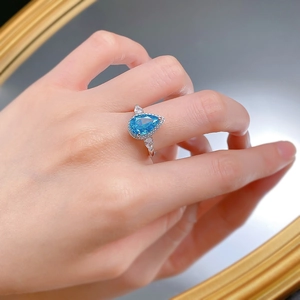 Macro shot of a pear-cut blue gemstone ring on a finger with elegant mirror reflections