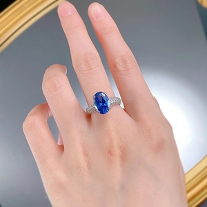 Gros plan d'une bague saphir bleu royal avec halo de diamants sur un doigt féminin