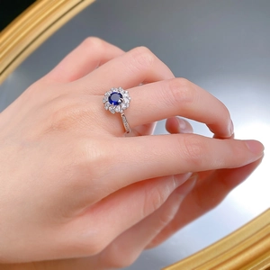 Detail of flower shaped S925 silver ring with blue sapphire and white zircon halo on finger