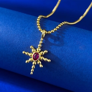 Macro detail of gold starburst pendant with an oval red gemstone on a blue display