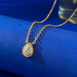 Macro detail of gold pear-shaped pendant with white stones on navy background