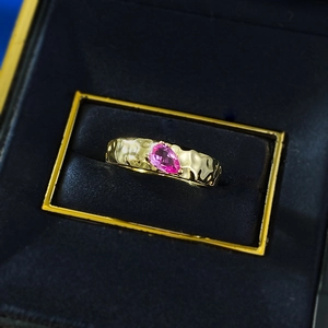 Detail of pink pear-cut gemstone ring with textured hammered gold band in a blue jewelry box