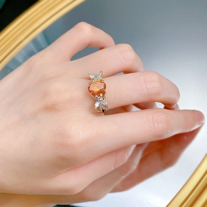 Detailed view of an oval orange gemstone ring with bow accents on a hand model