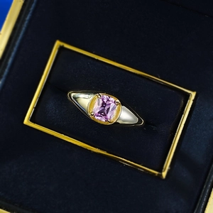 Macro detail of rectangle pink gemstone set in gold signet ring on blue velvet