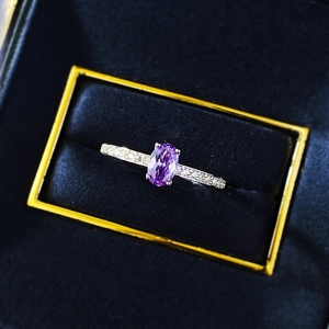 Close-up of oval purple gemstone ring with side stones in a blue velvet gift box