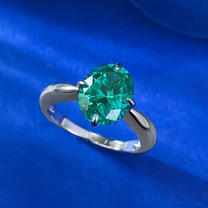 Oval cut green emerald ring with silver four-prong setting on dark blue texture