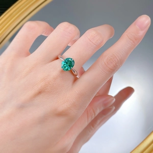 Macro detail of oval emerald gemstone ring with four-prong silver setting on hand