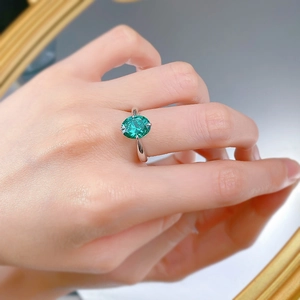 Macro shot of oval emerald green gemstone ring with silver four-prong setting on finger