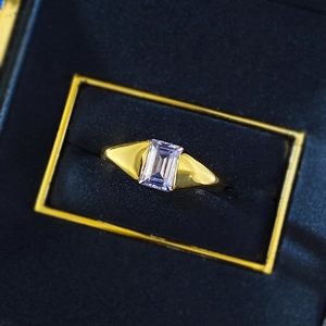 Macro shot of rectangular purple crystal ring set in gold band on blue velvet box