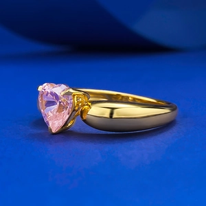 Macro d'une bague avec pierre rose en forme de cœur et anneau doré sur fond bleu
