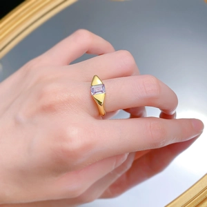 Macro detail of a gold geometric ring with a rectangular purple gemstone on a finger