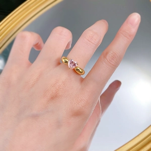 Détail d'une bague avec cristal rose en forme de cœur portée devant un miroir doré