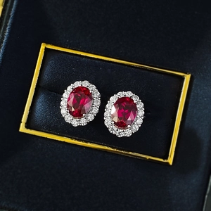 Close-up of halo-set oval ruby stud earrings presented in a luxury velvet jewelry box