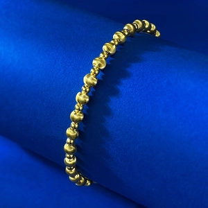 Macro detail of gold beaded bracelet with brushed and polished textures on blue display