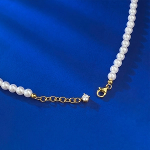 Détail d'un collier de perles blanches avec fermoir mousqueton doré et pendentif en zircon